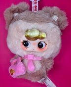 Brown plush hooded character with golden goggles and pink outfit with small pouch