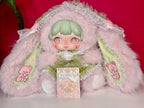Kawaii hooded plush doll in pink fur, green hair, holding a decorative blind box
