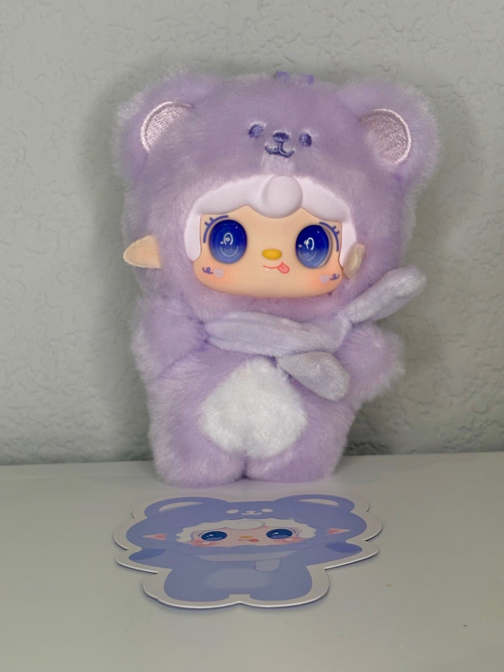 Lavender plush bear keychain with hood, paw details, and blue-eyed face
