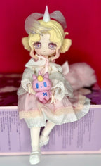 Horned ball-jointed doll holding a small pink cat pet, in white lace dress.