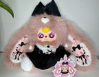 Pink fuzzy bunny plush in black dress with bow, long ears, and smiling face