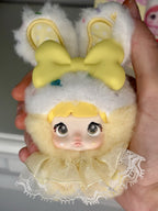 Plush bunny charm doll held in hand, yellow bow ears and cream lace dress