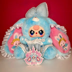 Blue-and-pink plush bunny doll with glittery eyes, lace ruffle dress, and crown badge