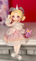 Ball-jointed doll sitting pose, blonde horn, white frilled dress and holding pink pet figure.