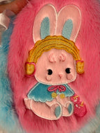 Pink-and-blue plush bunny hood with sleeping bunny face, gold headband, and felt ears