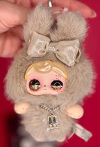 Beige plush keychain with gold bow, face charm, and hanging heart-tag charm necklace
