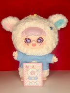 White plush lamb doll with blue shirt and lace collar, holding a pink character card