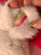 Cream plush doll paw with rainbow-striped sleeve cuff, close-up.