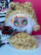 Collectible plush pendant doll with tan leopard hood, light hair, red-toned top, green eyes.