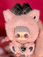 Collectible plush doll with light pink fur, gray cap, and purple-eyed face
