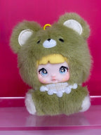 Nommi plush blind box figure: olive green bear hood, yellow top, baby doll face with big eyes