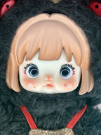 Articulated plush doll face with big blue eyes, blonde bangs, dark hood