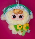 Light yellow plush baby doll with green lace hood trim and flower-themed chest, big eyes