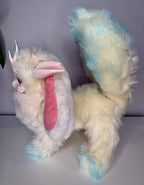 Fantasy creature plush lying sideways, long pink ears and silver antlers, cream and blue fur