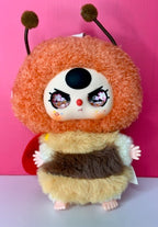 Collectible fuzzy plush character with orange fur, dark eyes, and brown-and-cream scarf