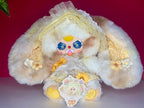 White and yellow plush doll with ruffled hood, lace dress, and smiling face