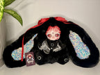 Black plush bunny doll in resting pose with red bow, rainbow-speckled ears, and hang tag