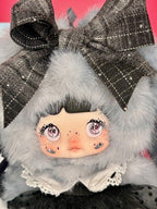 Close-up gray plush designer doll face with big plaid bow and fluffy hood