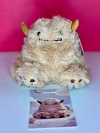 Tan fuzzy plush monster seated with small horns and stitched closed mouth
