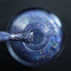 Holographic glitter nail polish bottle with brush holding purple rainbow sparkles