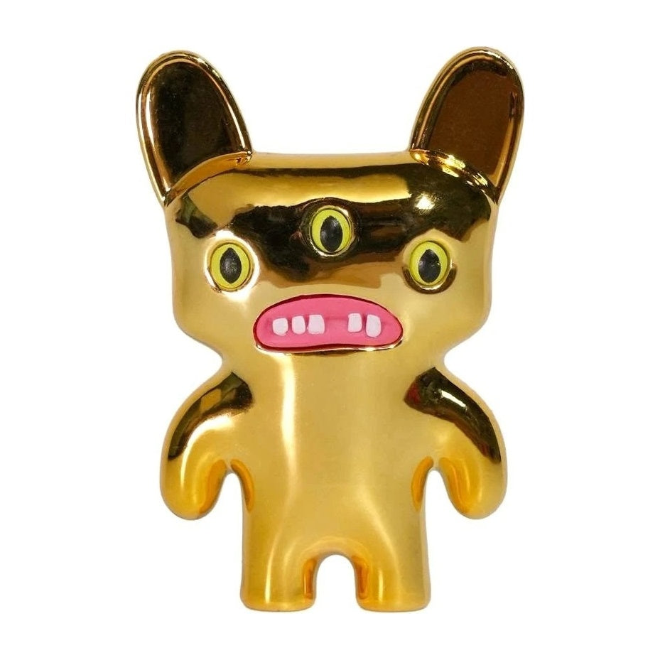 Gold cat-like monster figure with green eyes and a wide pink-tooth grin