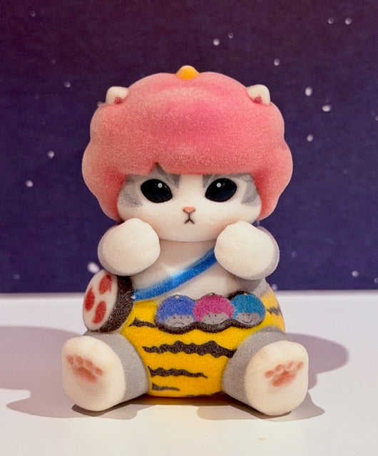 Sitting plush cat figure with pink hood, big eyes, blue scarf, yellow striped outfit
