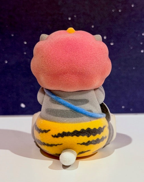 Pink cat-like flocked figure in blue scarf, striped outfit, sitting pose