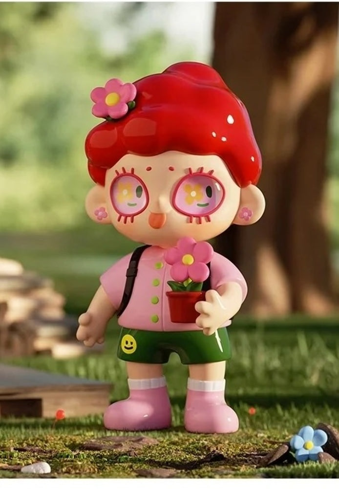 Red-haired girl blind box figure with flower hair clips, pink top, green skirt, holding a book