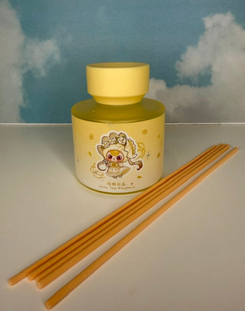 Yellow ceramic reed oil diffuser with two light wooden reeds and character design on jar