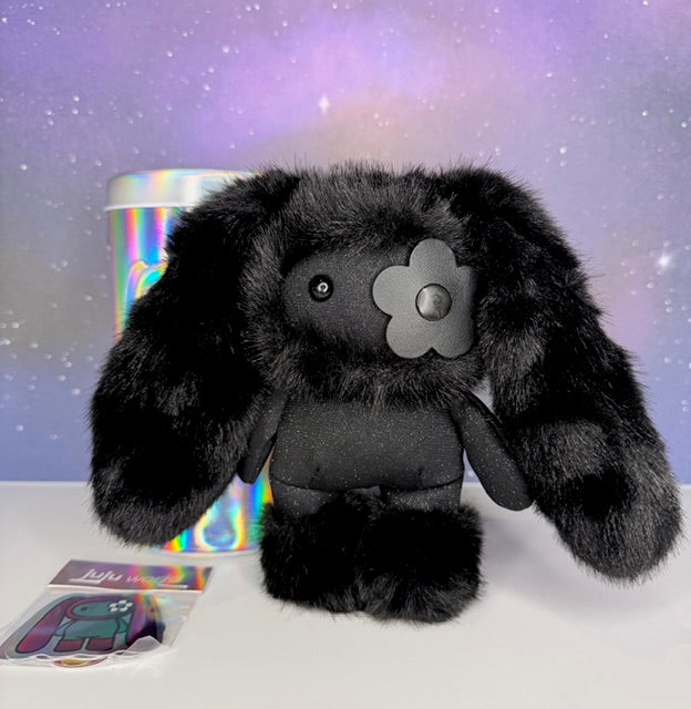 Black plush rabbit bag charm with metal flower face badge, sitting pose next to tin