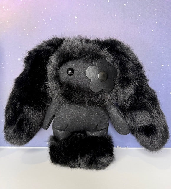 Front view of black plush rabbit bag charm with metal flower badge and round eyes