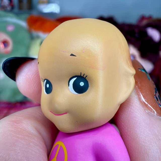 Close-up of pink mini figurine face and purple shirt, held in a hand