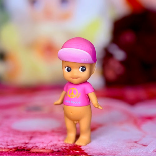 Front view pink mini figurine with purple cap and peace symbol shirt