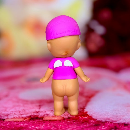 Pink mini figurine with purple shirt and white peace symbol on chest, standing on fabric