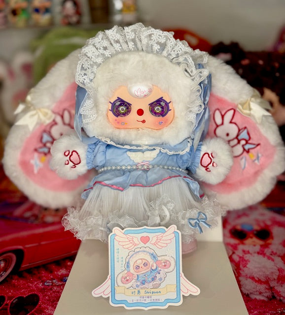 Plush baby figure in blue dress holding a blue heart-themed card with cute character art