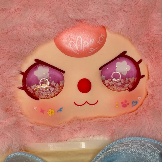 Pink plush figure face with purple glitter eyes, flower details, and smile