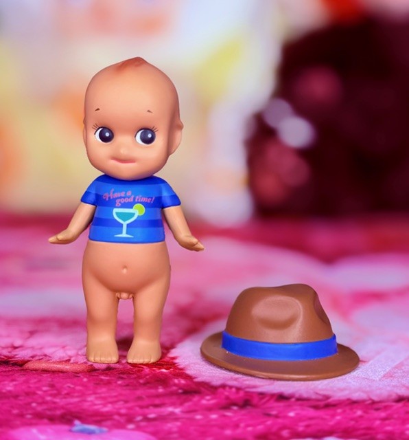 Toy angel figure with blue shirt beside brown fedora hat on pink fabric