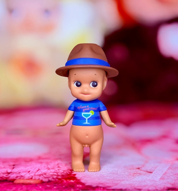 Small toy angel figure facing camera with blue shirt and brown hat, big eyes