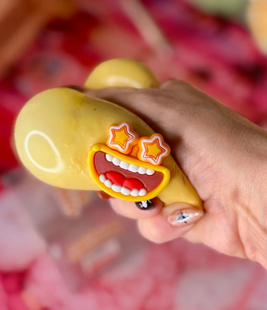 Yellow potato-shaped squishy toy with silly open-mouth face and star eyes, held in hand