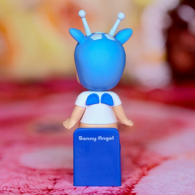 Blue sitting vinyl figurine with antennae, open hands, and blue letter O on outfit