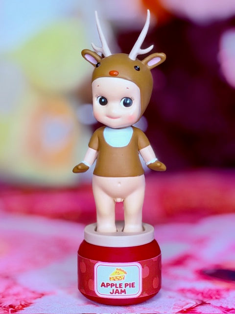 Reindeer character figurine facing front, white antlers, brown outfit, red base with Apple Pie Jam