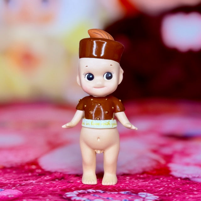 Small vinyl doll figurine facing forward, brown hat and jacket with light pants