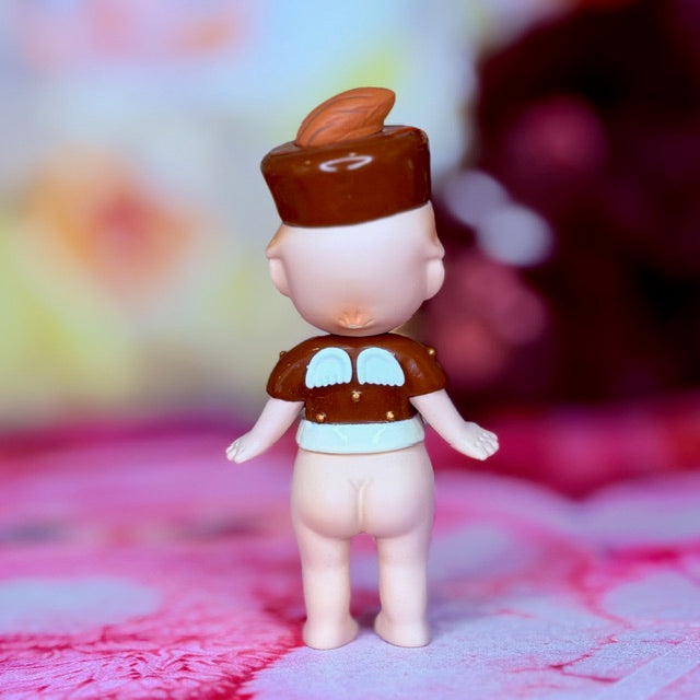 Small vinyl doll figurine with brown hat and outfit, holding arms at sides