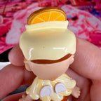 Small Sonny Angel figurine with orange slice hat, white outfit, and cream shoes