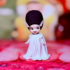 Custom vinyl doll figure with dark purple hair, white bride outfit, seated with relaxed face.