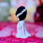 Custom vinyl doll side view with dark purple hair, white headband, white dress and hands.