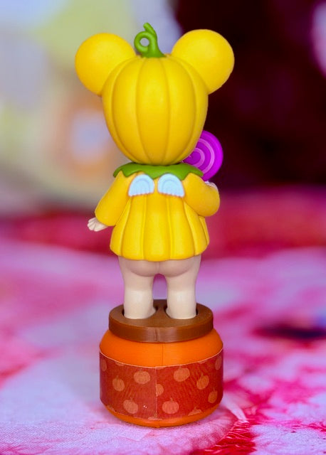 Yellow mouse figurine with pumpkin outfit, standing on round base with purple lollipop.