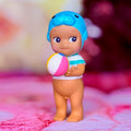 Manatee-style toy figure holding a pink-and-white beach ball, blue hat, tan body